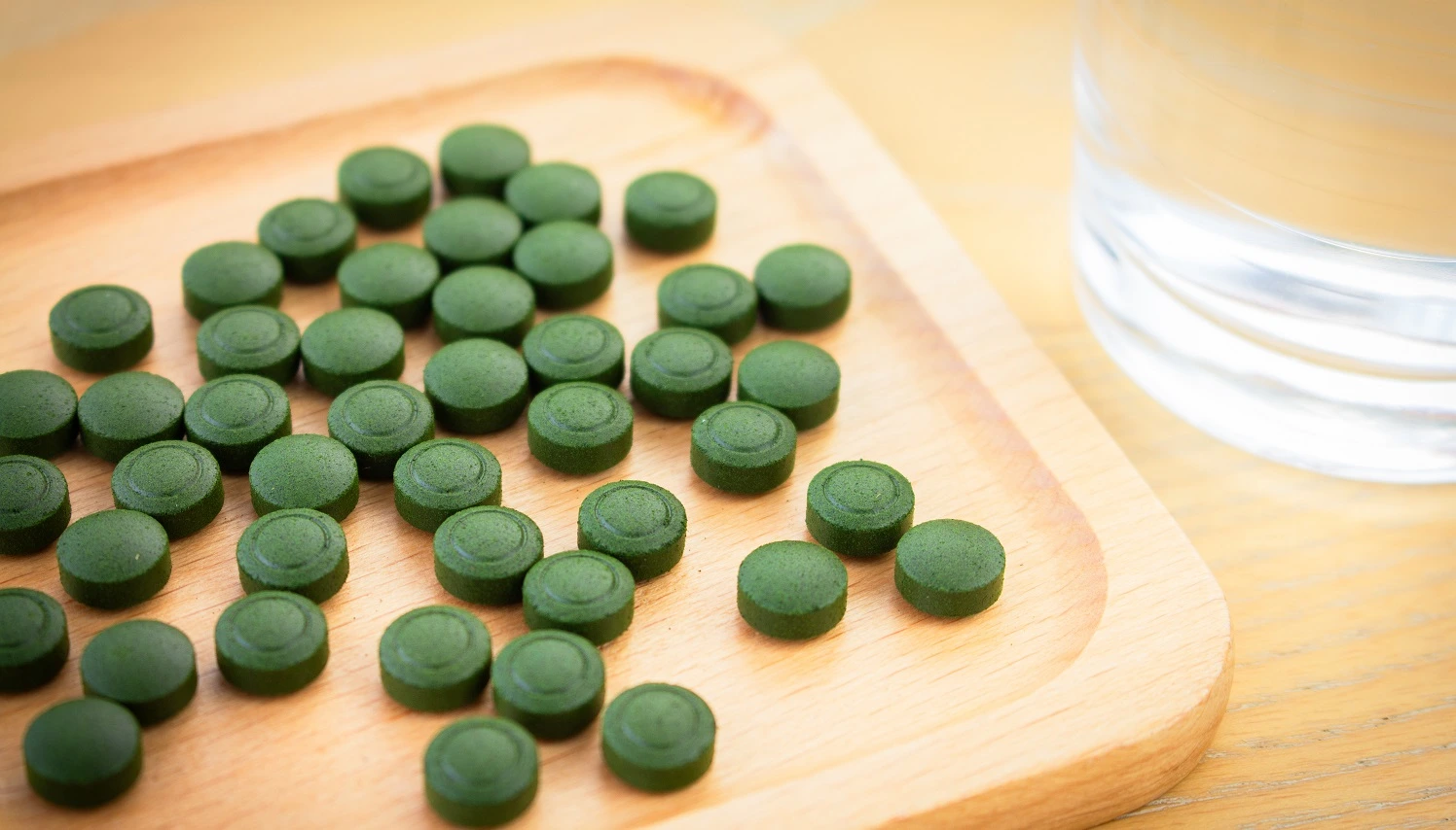 A bunch of chlorella tablets on a wooden dish and a glass of water