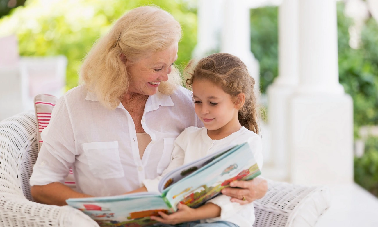 Woman is reading a book to her grandaughter in the yard